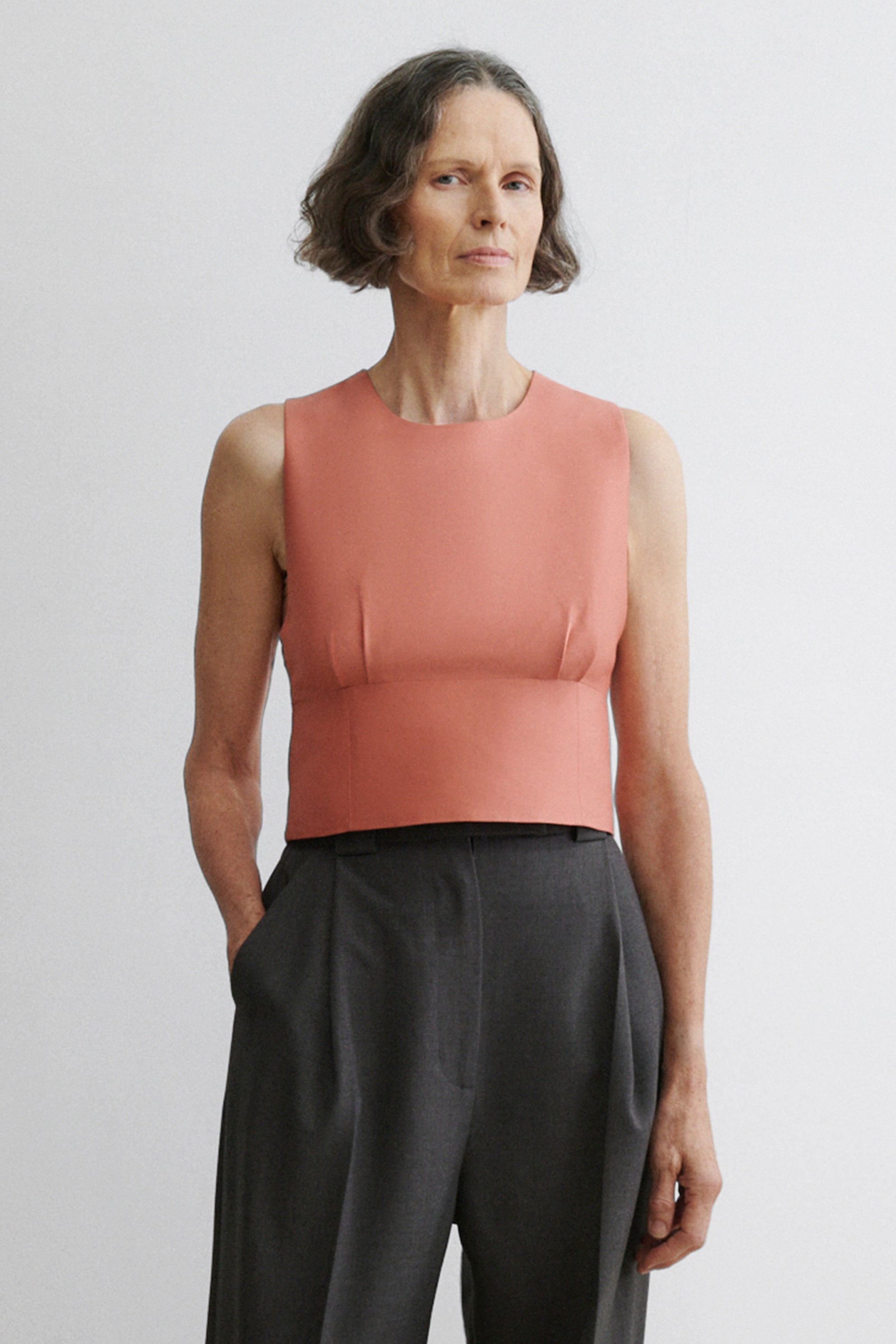 Woman wearing a pink sleeveless top and black pants against a plain background
