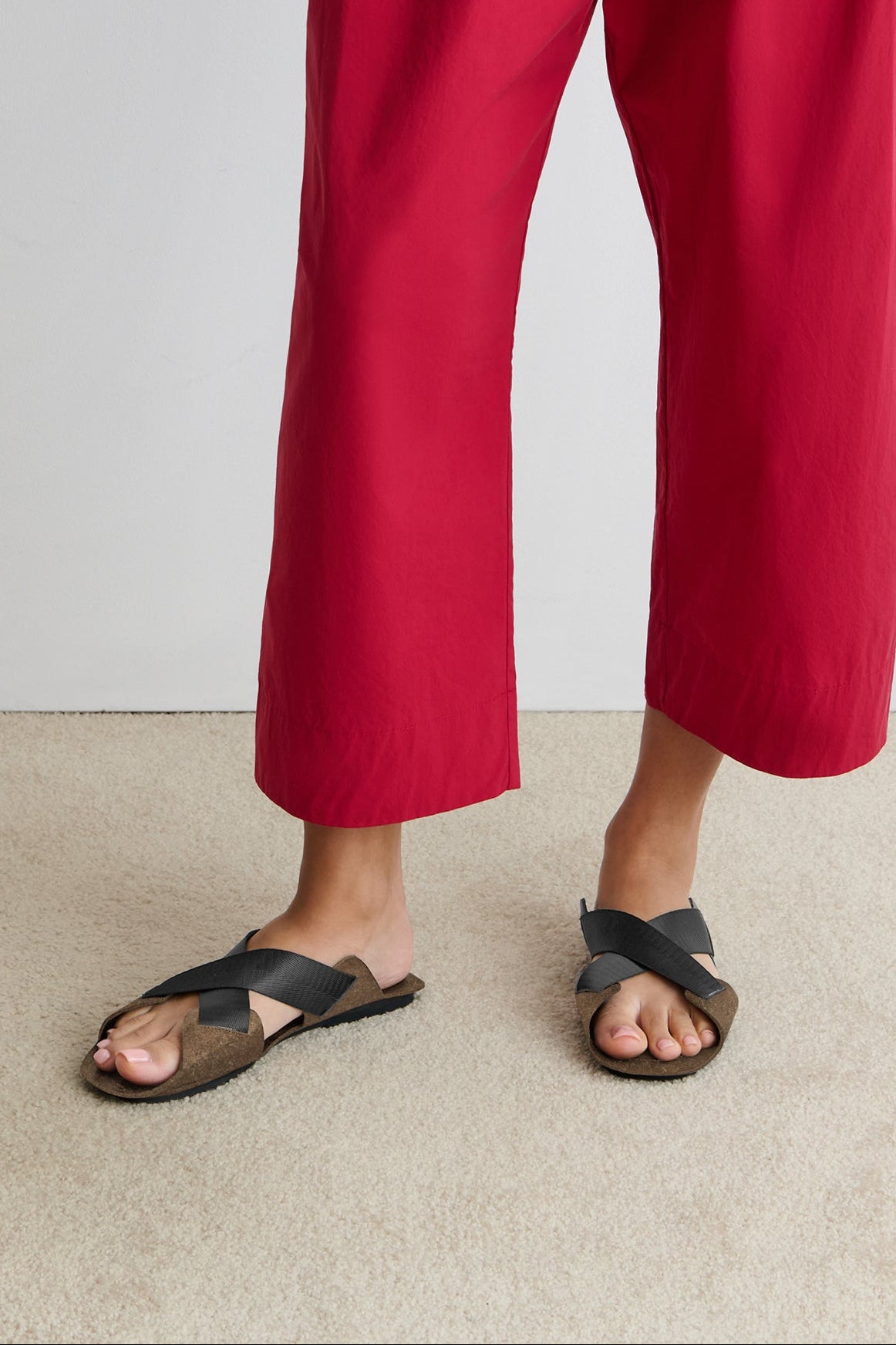 Person wearing red pants and black sandals on a plain background