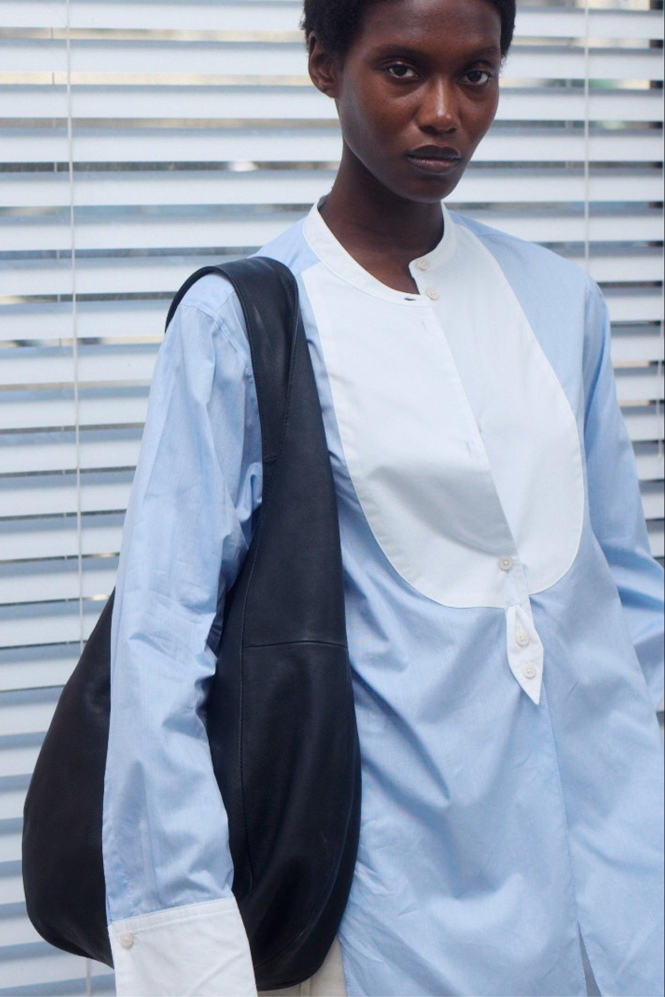 Person wearing a light blue shirt with a white collar against a striped background