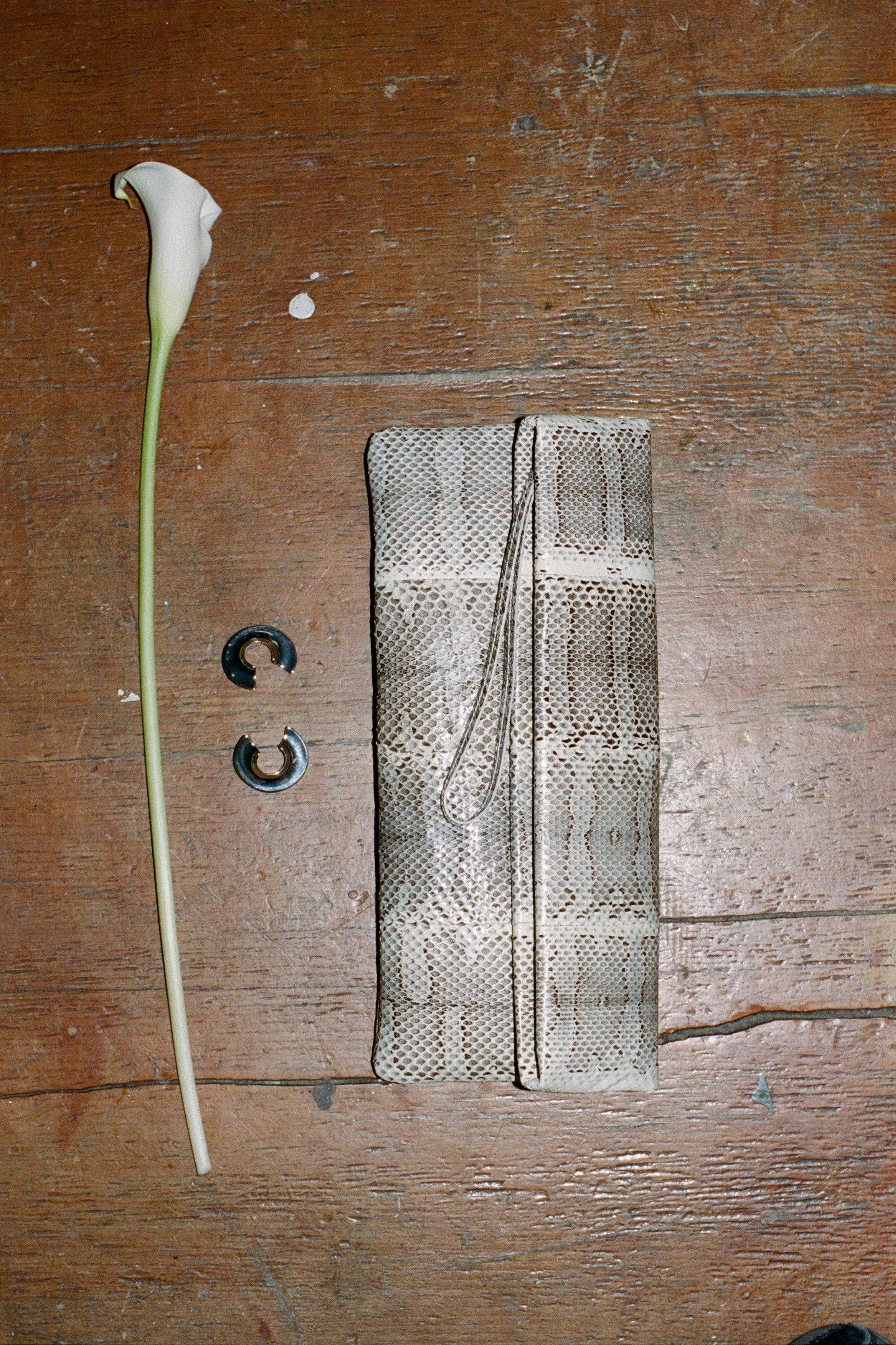 Rachel Comey Snakeskin Pillow Clutch handbag on a table next to earrings and a lily flower